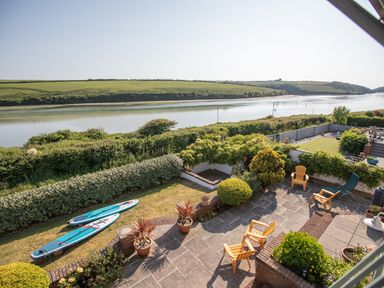 A patio with chairs and plants overlooking a river with grassy hills in the background at Newquay Tamarisk Lodge on the Gannel in Newquay