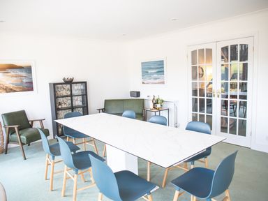 A dining room with a white rectangular table surrounded by blue chairs and green armchairs at Newquay Tamarisk Lodge on the Gannel in Newquay