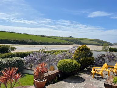 A garden patio with yellow chairs and potted plants overlooking a river and green hills at Newquay Tamarisk Lodge on the Gannel in Newquay