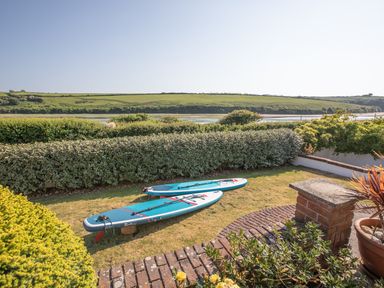 Two paddle boards on a grassy garden next to brick paving with shrubs and a river and hills in the background at Newquay Tamarisk Lodge on the Gannel in Newquay