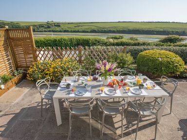 An outdoor dining table set for breakfast with chairs flowers and a scenic view of green hills at Newquay Tamarisk Lodge on the Gannel in Newquay