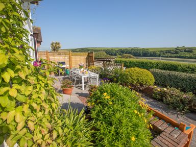 A garden patio with a dining table set for a meal surrounded by plants and bushes at Newquay Tamarisk Lodge on the Gannel in Newquay