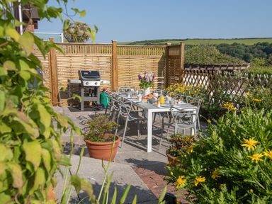 An outdoor patio with a dining table set for breakfast and a barbecue grill at Newquay Tamarisk Lodge on the Gannel in Newquay