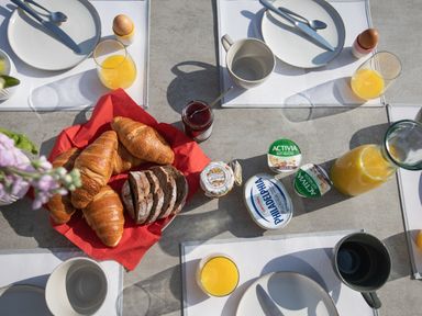 A breakfast table with croissants, sliced bread, eggs, orange juice, yogurt, cream cheese, jam, and cutlery at Newquay Tamarisk Lodge on the Gannel in Newquay