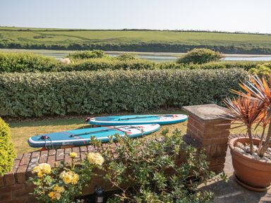 Two paddleboards on grass behind a brick wall with plants and a potted plant near the patio at Newquay Tamarisk Lodge on the Gannel in Newquay