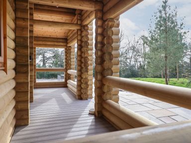 A wooden log porch overlooking a grassy area with trees at Redwood Lodge in Ellesmere