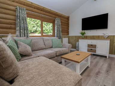 A living room with a beige sofa with green pillows a wooden coffee table and a white cabinet with a television on the wall at Redwood Lodge in Ellesmere