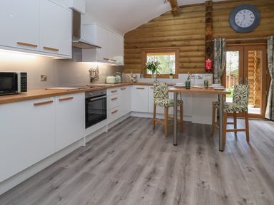 A kitchen with white cabinets wooden countertops and two patterned chairs at Redwood Lodge in Ellesmere