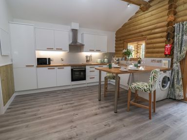 A kitchen with white cabinets wooden countertops a built in oven microwave washing machine and a small dining table with two chairs at Redwood Lodge in Ellesmere