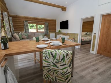 An open living room and kitchen area with a wooden dining table set with plates and glasses and a sofa near window at Redwood Lodge in Ellesmere