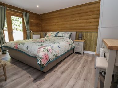 A bedroom with a double bed with floral bedding two bedside tables with lamps a wooden floor and a wardrobe at Redwood Lodge in Ellesmere