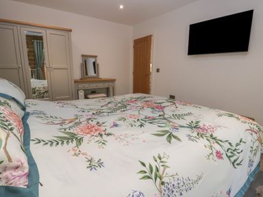 A bedroom with a floral bedspread a wardrobe a vanity table and a wall-mounted television at Redwood Lodge in Ellesmere
