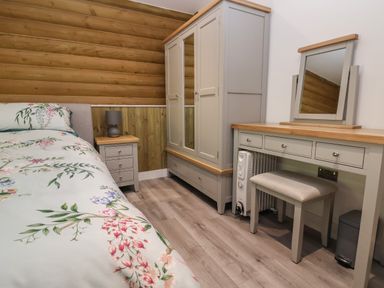 A bedroom with a bed floral bedding a bedside table with lamp a wardrobe and a dressing table with a mirror and stool at Redwood Lodge in Ellesmere
