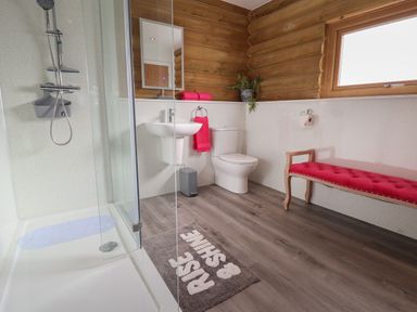A bathroom with a shower stall sink toilet pink bench and wooden walls at Redwood Lodge in Ellesmere