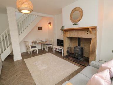 A living room with a wood-burning stove fireplace a dining table with chairs a gray sofa and a beige rug at Cosy Cottage in Amble