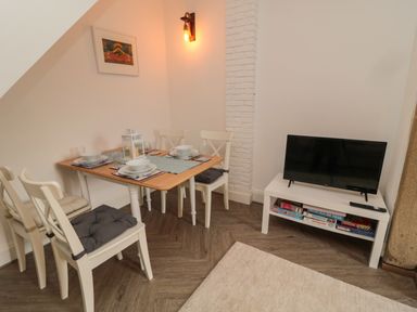 A dining table set for four with chairs and cushions next to a TV on a white stand with board games underneath at Cosy Cottage in Amble