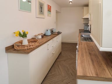A galley kitchen with wooden countertops yellow flowers toaster and kettle on the counter at Cosy Cottage in Amble