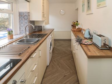 A kitchen with wooden countertops and white cabinets a washing machine a toaster a kettle and a sink at Cosy Cottage in Amble