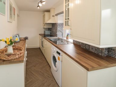A galley kitchen with wooden countertops appliances and flowers in a jug at Cosy Cottage in Amble