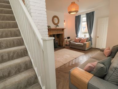 A living room with two gray sofas and pink cushions a fireplace and stairs at Cosy Cottage in Amble