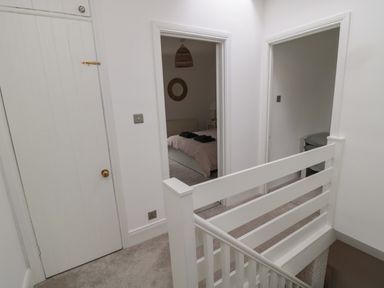 A hallway with white walls and carpet leading to two open bedrooms at Cosy Cottage Amble