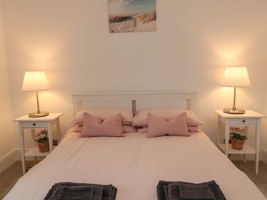 A bedroom with a bed between two nightstands with lamps and flowers at Cosy Cottage in Amble