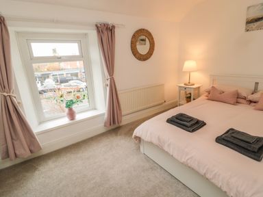 A bedroom with a bed beside a window with curtains and a bedside table with a lamp at Cosy Cottage in Amble
