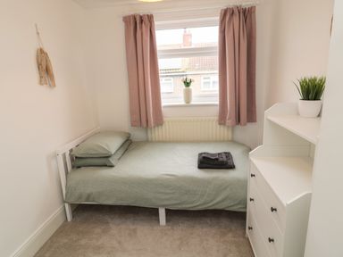 A small bedroom with a single bed next to a window with curtains and a white dresser with a plant on top at Cosy Cottage in Amble