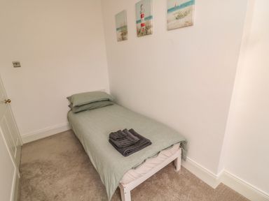 A small bedroom with a single bed green bedding and folded towels on the bed at Cosy Cottage in Amble