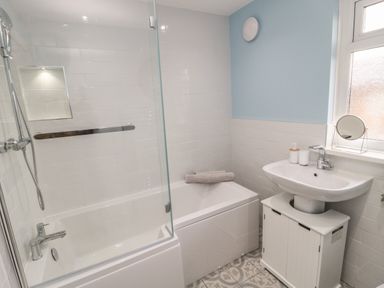 A bathroom with a bathtub shower combination sink on a cabinet and a towel on the bathtub at Cosy Cottage in Amble