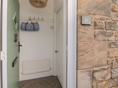 A partially open green door showing a hallway with coat hooks a rolled bag radiator and a white door at Cosy Cottage in Amble