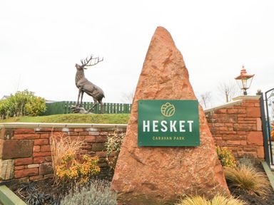A large rock with a Hesket Caravan Park sign near a stag statue and a brick wall at Rosie's Zen Den in High Hesket near Armathwaite