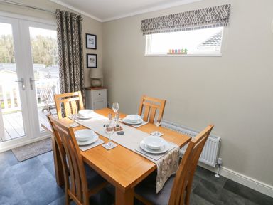 A dining room with a wooden table set for four near a window and glass doors at Lodge 53 in Stepaside near Kilgetty