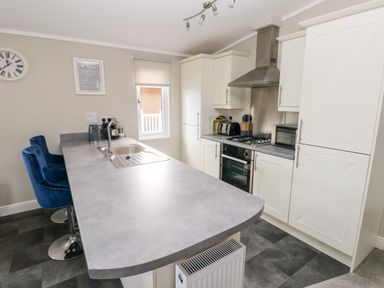 A kitchen with white cabinets a gray countertop a sink a stove a toaster a microwave and two blue bar stools at Lodge 53 Stepaside near Kilgetty