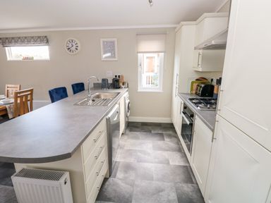 A kitchen with a countertop, sink, dishwasher, oven, stove, and dining table with chairs at Lodge 53 in Stepaside near Kilgetty