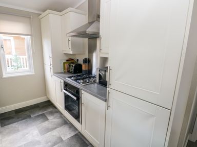 A kitchen with white cabinets a countertop a gas stove an oven a toaster a knife block and a window at Lodge 53 Stepaside near Kilgetty