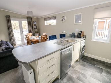 A kitchen and dining area with a sink, dishwasher, washing machine, dining table with chairs, and sofa at Lodge 53 Stepaside near Kilgetty