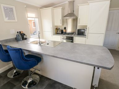 A kitchen with a grey countertop island with a sink and two blue chairs with backs at Lodge 53 Stepaside near Kilgetty
