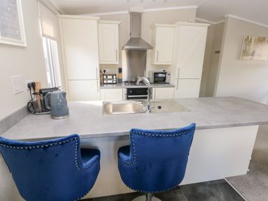 A kitchen with white cabinets a stainless steel sink blue bar stools and appliances at Lodge 53 Stepaside near Kilgetty