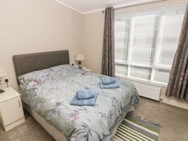 A bedroom with a double bed with floral bedding two bedside tables with lamps a window with blinds and curtains and a striped rug on the floor at Lodge 53 Stepaside near Kilgetty