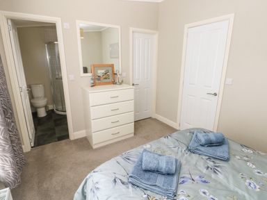 A bedroom with a bed with folded towels a white chest of drawers a mirror and a door to a bathroom at Lodge 53 Stepaside near Kilgetty