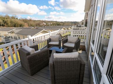 An outdoor balcony with four wicker chairs around a small table overlooking rooftops and countryside at Lodge 53 Stepaside near Kilgetty