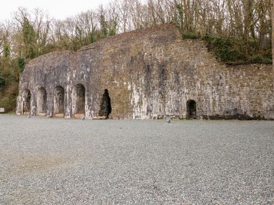 A stone structure with arched openings and gravel ground in front surrounded by trees at Lodge 53 in Stepaside near Kilgetty