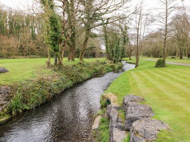 A narrow stream flowing between grassy banks with trees and rocks alongside at Lodge 53 in Stepaside near Kilgetty