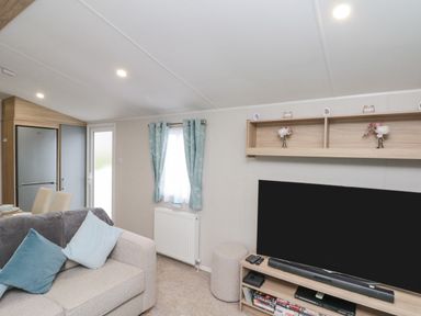 A living room with a sofa, television, shelving unit, curtains, and a refrigerator at Rowan Court 2 in Cayton