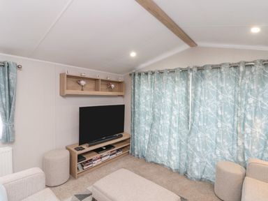 A small living room with a television on a wooden stand and patterned blue curtains at Rowan Court 2 in Cayton