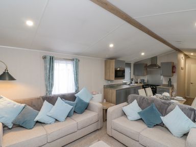 A seating area with two sofas and blue cushions next to a kitchen and dining area at Rowan Court 2 in Cayton