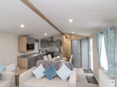 An open plan living room and kitchen with beige sofas and blue cushions at Rowan Court 2 in Cayton