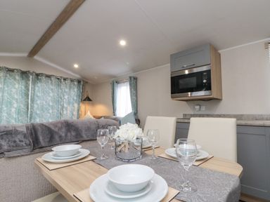 A dining table set with plates glasses and a flower vase next to a kitchen area with a microwave oven at Rowan Court 2 in Cayton