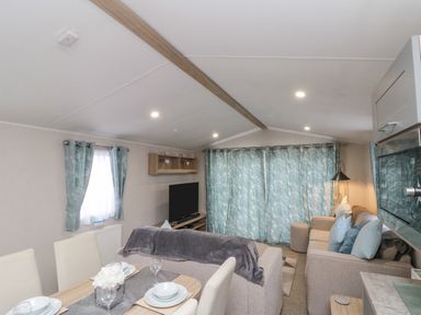 A living room with sofas dining table and TV with blue curtains at Rowan Court 2 in Cayton